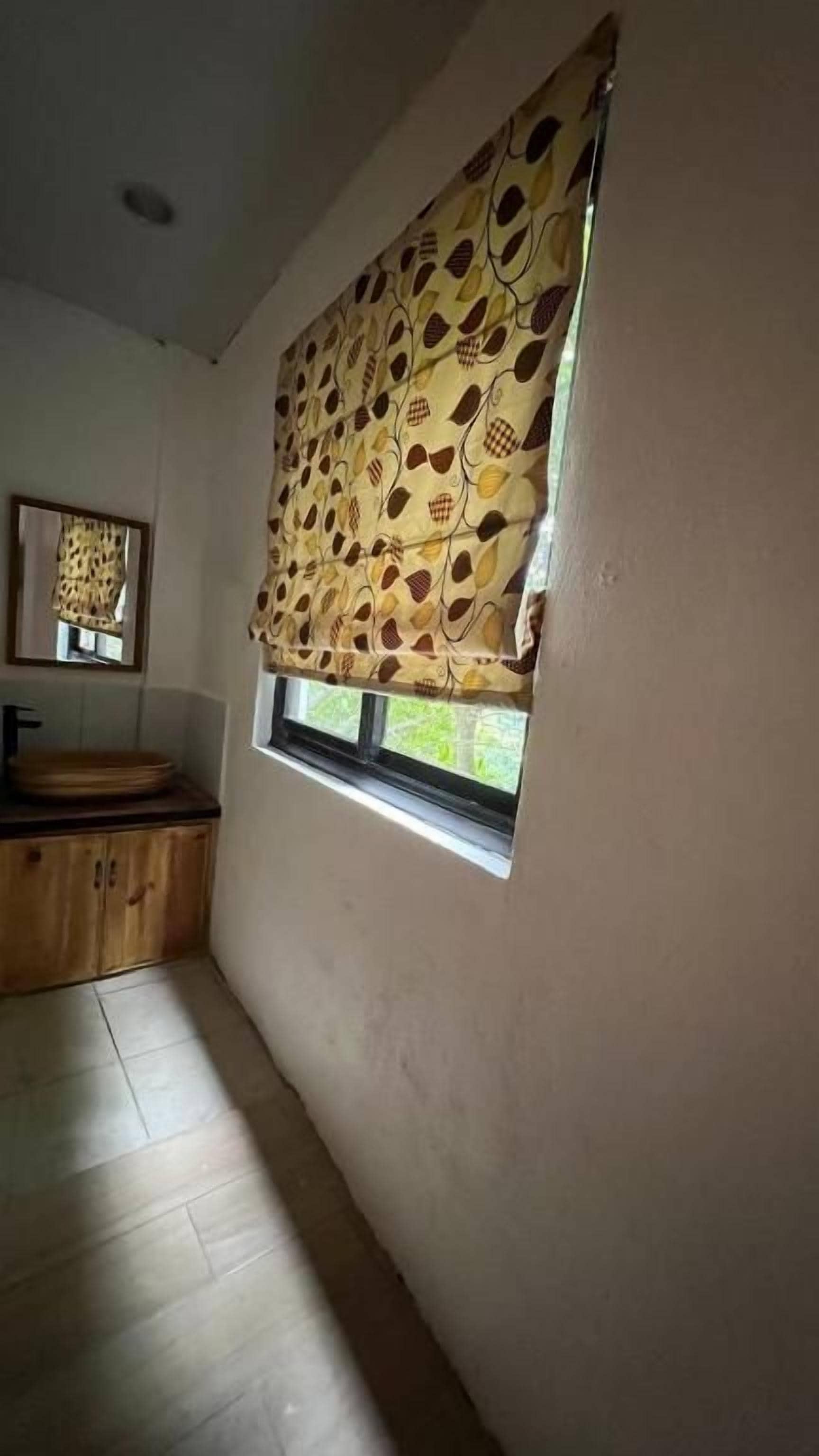 Habitació amb finestra coberta per una cortina amb dibuixos, un armari de fusta i una petita finestra.