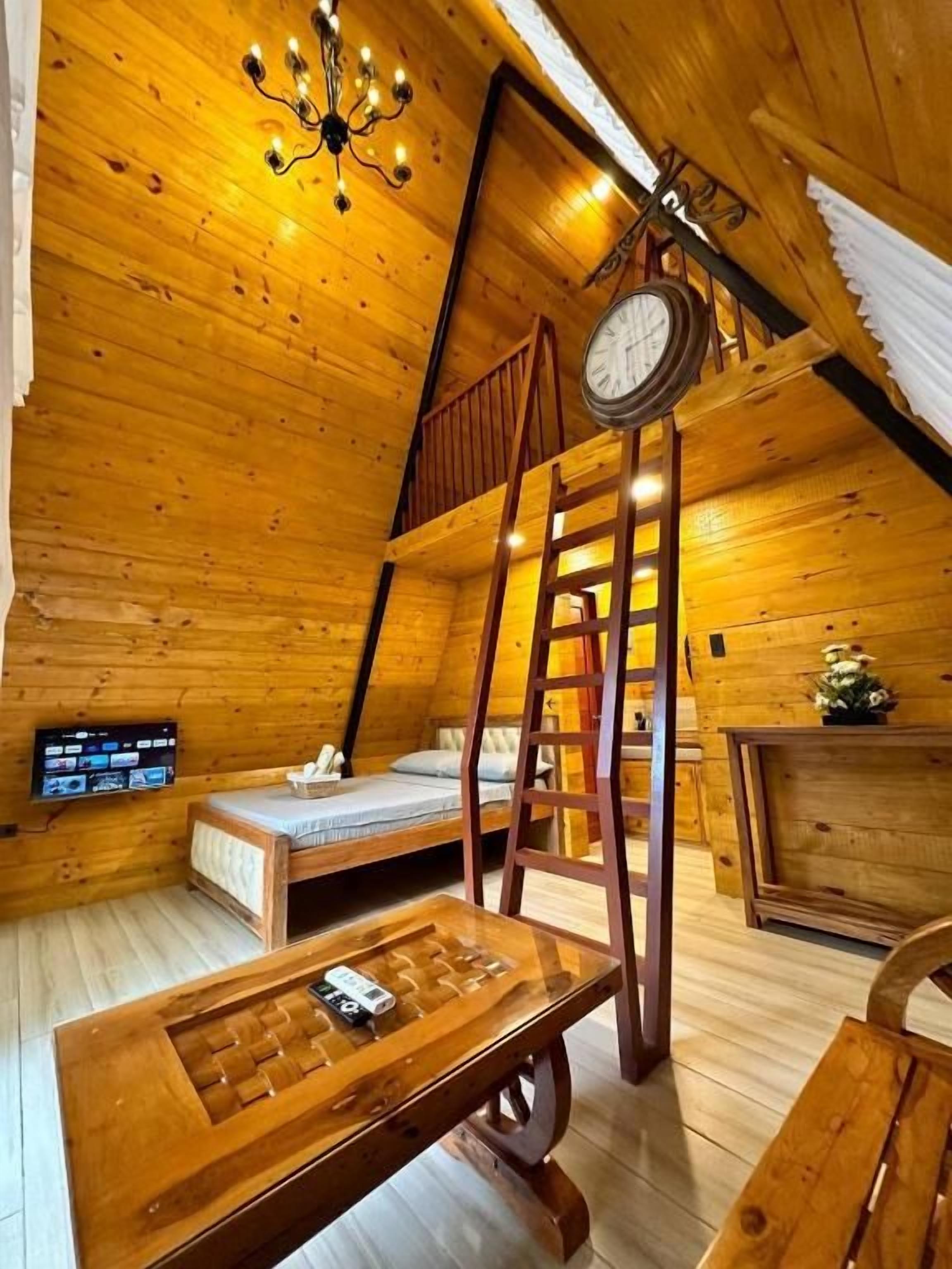 Una habitació de fusta acollidora amb un llit de pallera, una escala de fusta, una taula de fusta i un rellotge a la paret.