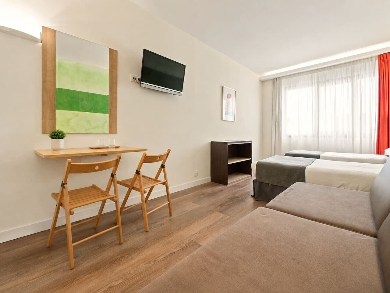 Ein modernes Wohnzimmer mit einem Holztisch, zwei Stühlen, einem Flachbildfernseher, einer Sofagarnitur und einem großen Fenster mit transparenten Vorhängen.