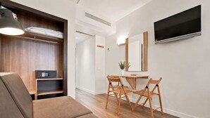 Uma sala de estar moderna com sofá, mesa de jantar com cadeiras, TV fixada na parede e um armário de madeira.