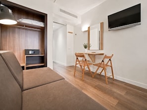 Ein modernes Wohnzimmer mit Sofa, Esstisch mit Stühlen, einem an der Wand befestigten Fernseher und einem Holzkasten.