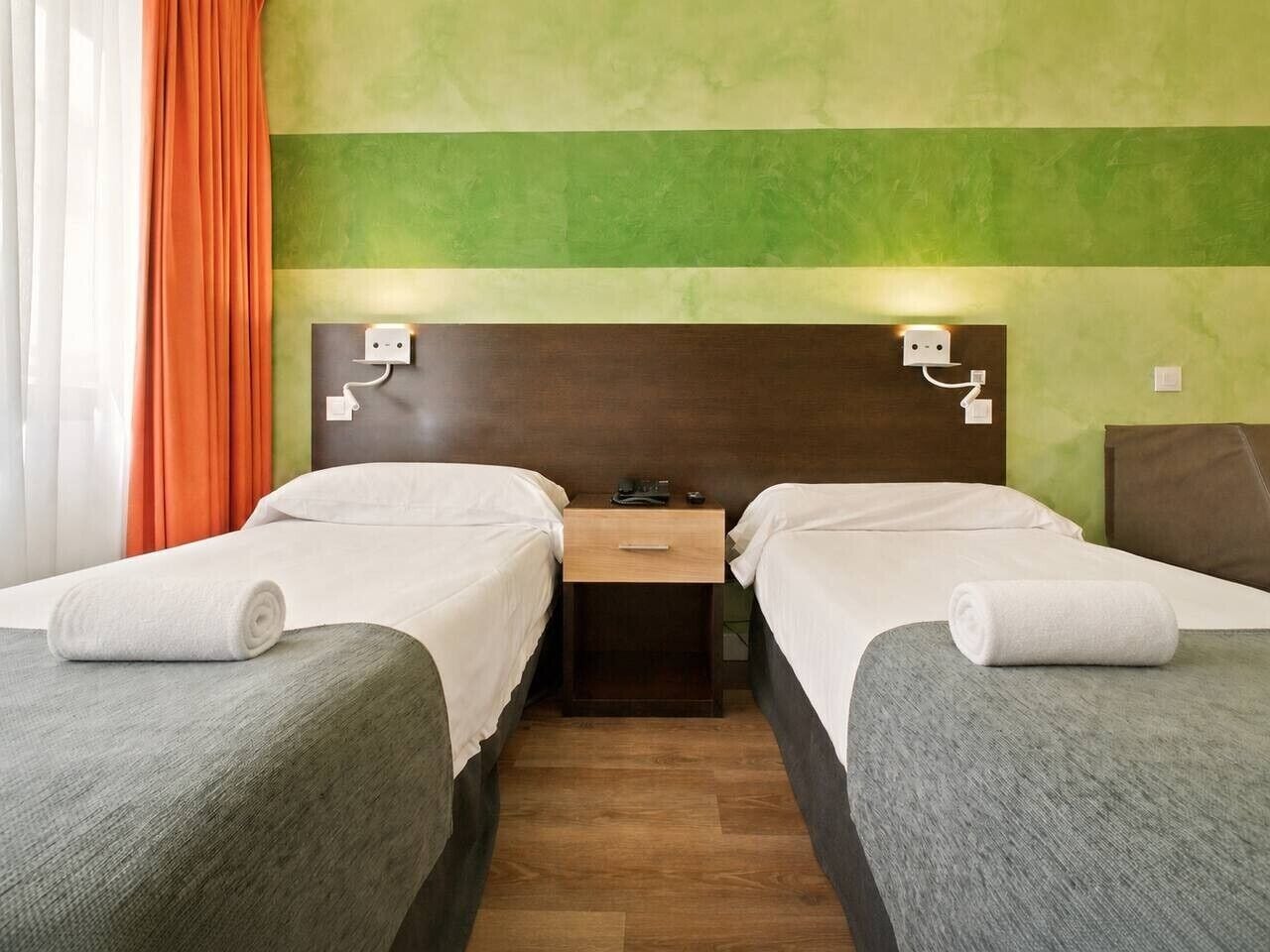 Une chambre d’hôtel avec deux lits, une table de chevet et un mur vert.
