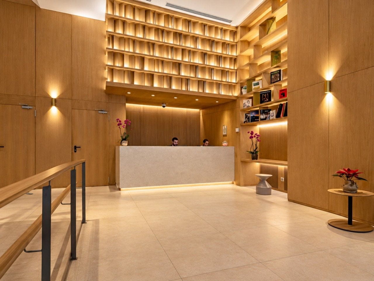 A reception area with a wooden reception desk, a seating area with a small table, and a wall with shelves containing books and decorative items.