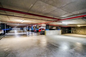 Eine mehrgeschossige Tiefgarage mit Betonpfeilern, roten Rohren und ausgewiesenen Parkplätzen.