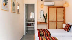 Una habitación de hotel con cama, mesitas de noche, un espejo, armario y puerta que da a un baño.