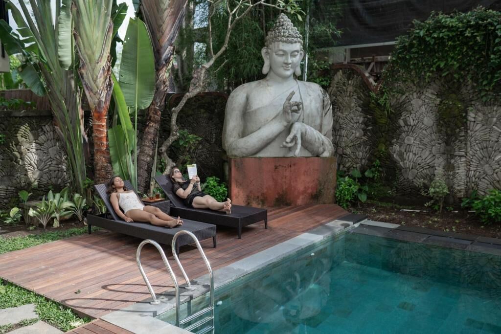 A statue of a seated figure in a garden setting with a pool and lounge chairs.