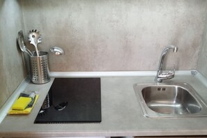 Eine Küche mit Spüle aus Edelstahl, Schneidebrett in Schwarz, einem gelben Schwamm und einem Metall-Utensilienhalter.
