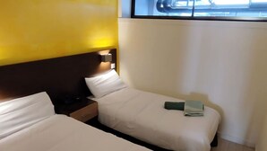 Et hotelværelse med to senge, et natbord og et vindue med persienner.