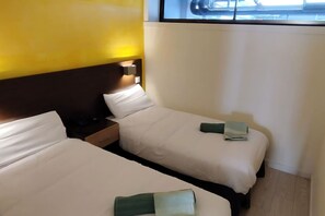 Ein Hotelzimmer mit zwei Betten, einem Nachttisch und einem Fenster mit Jalousien.