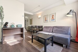 A modern living room with a sofa, a coffee table, a dining area with chairs, a kitchen counter with appliances, and a wall-mounted lamp. - Comfort and functionality right next to the Retiro Park (Madrid)