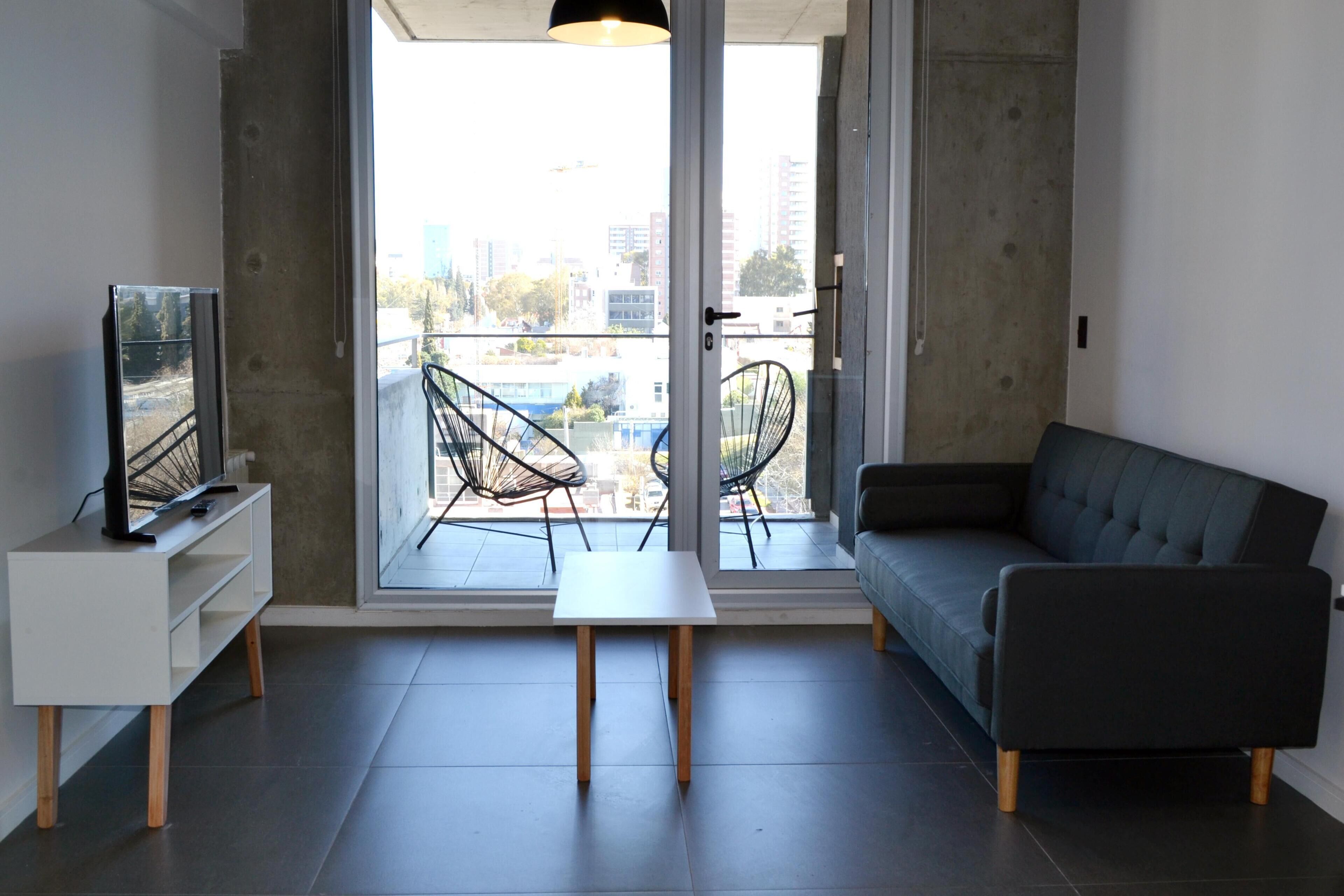 A modern living room with a sofa, a TV, and a balcony with chairs.