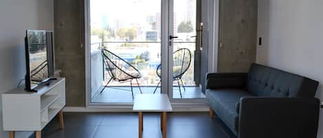 A modern living room with a sofa, a TV, and a balcony with chairs.