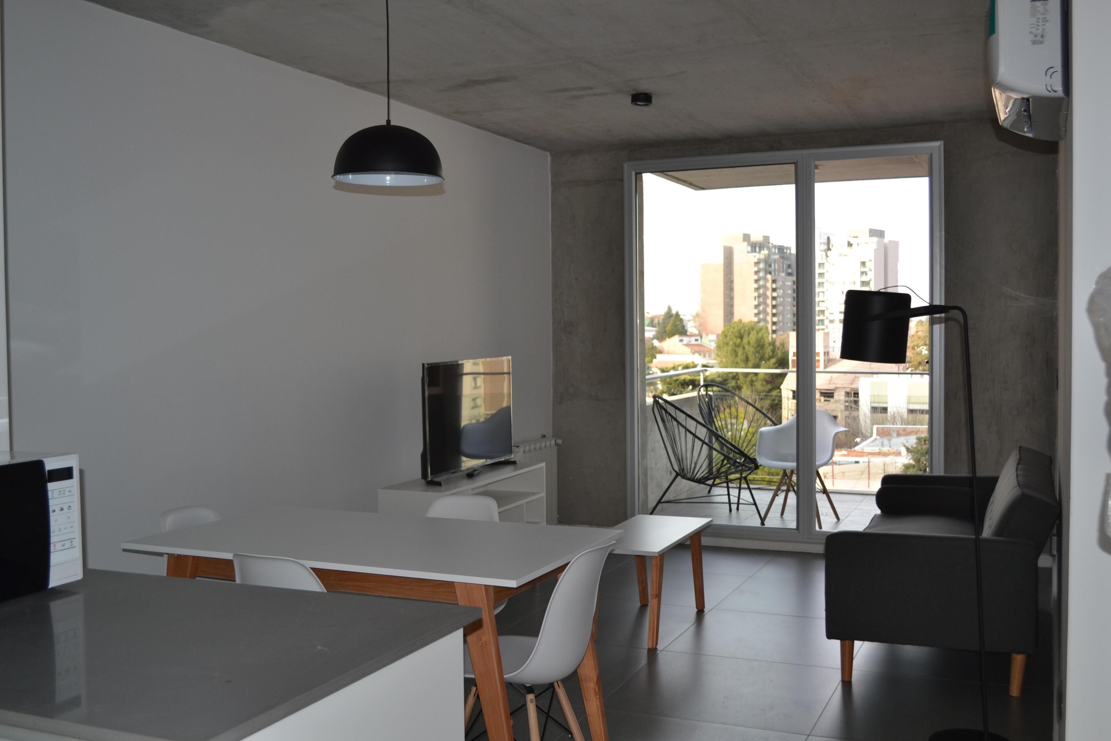 Un espacio habitable moderno con comedor, televisor de pantalla plana y balcón con vistas a la ciudad.