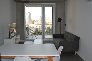 A modern living space with a dining area, a sofa, a TV, and a balcony with a view of buildings.