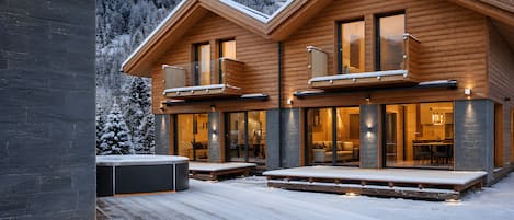 A two-story wooden cabin with a balcony, large windows, and a deck.