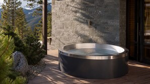 Un jacuzzi en una terraza de madera con un muro de piedra y vistas a la montaña al fondo.