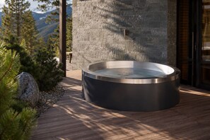 Un jacuzzi en una terraza de madera con un muro de piedra y vistas a la montaña al fondo.