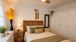 Une chambre à coucher comprenant un lit, des tables de chevet, un ventilateur de plafond, un miroir et une armoire.