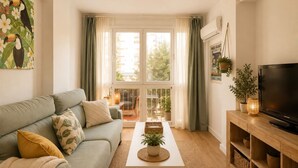 Un salon comprenant un canapé, une table basse, un téléviseur et un balcon avec des rideaux.