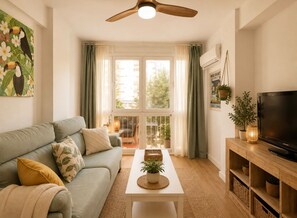 A living room with a sofa, a coffee table, a TV, and a balcony with curtains. - Terrasol Berlin 2 in Torre del Mar (Velez-Malaga)