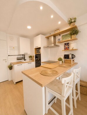 A modern kitchen with white cabinetry, a wooden island, and a breakfast bar with white chairs. - Terrasol Berlin 2 in Torre del Mar (Velez-Malaga)