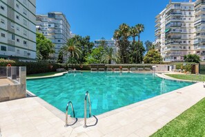 A swimming pool with a clear blue water, surrounded by a tiled deck, and adjacent to high-rise residential buildings. - Terrasol Berlin 2 in Torre del Mar (Velez-Malaga)