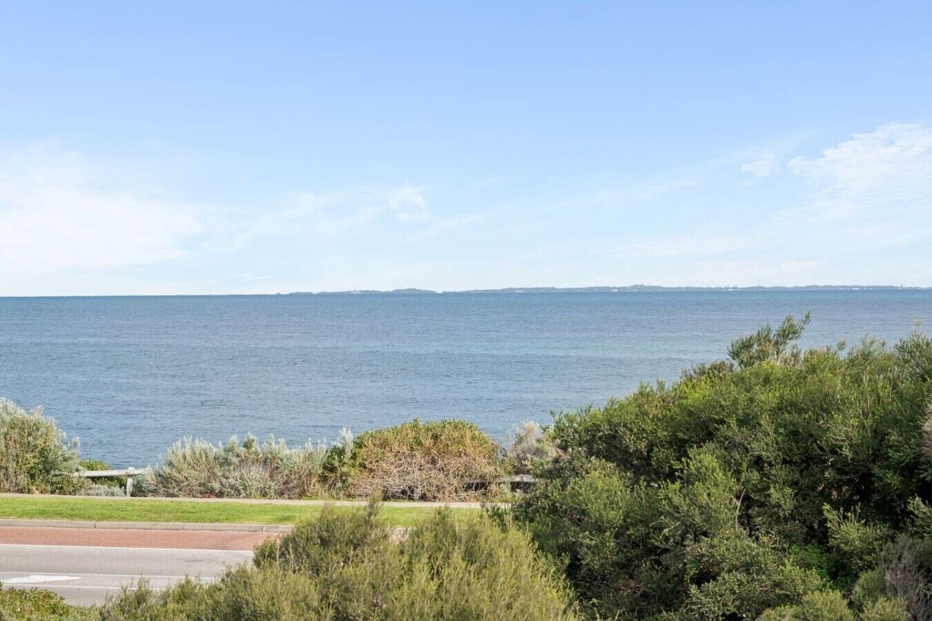 A coastal view with a clear sky, a body of water, and dense greenery in the foreground.