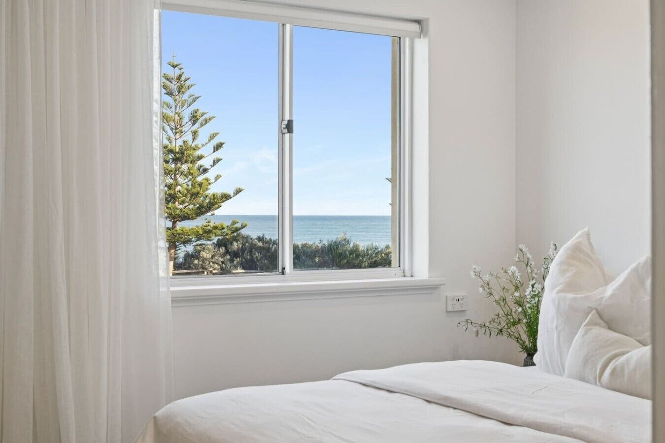 Ein Schlafzimmer mit großem Fenster, weißer Bettwäsche und Meerblick.