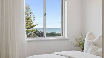 Ein Schlafzimmer mit großem Fenster, weißer Bettwäsche und Meerblick.