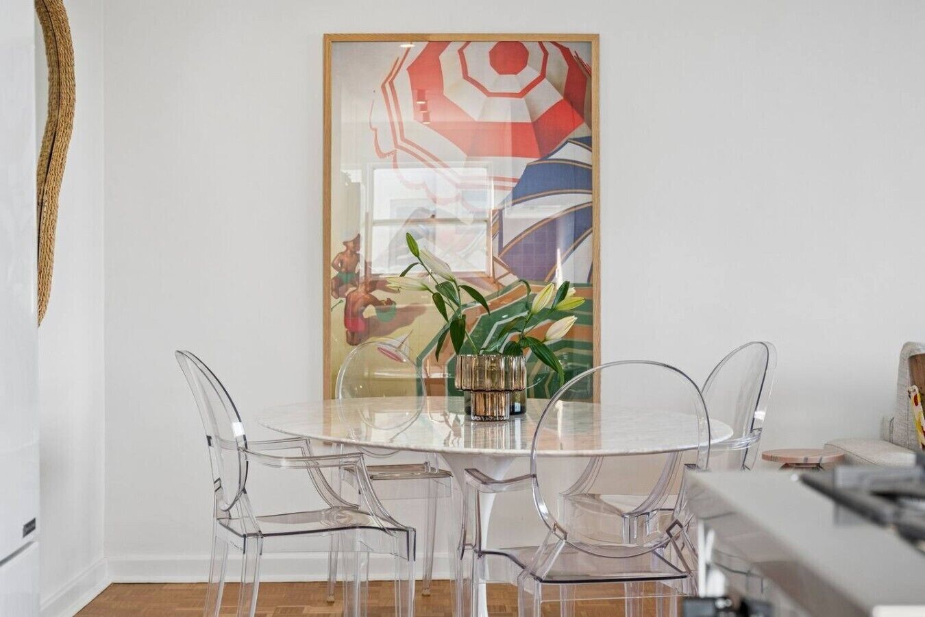 A modern dining area with a glass table and chairs, a vase with flowers, and a colorful abstract painting on the wall.