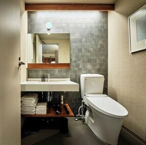 Ein Badezimmer mit weißer Toilette, einem Waschbecken mit Spiegel darüber und einer gefliesten Rückwand.