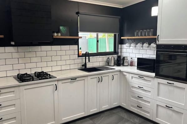 A kitchen with white cabinets, a black countertop, and a window with a view. - Family retreat in Ningi. Pet friendly! (Ningi)
