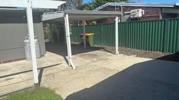 A covered outdoor area with a green fence, a concrete patio, and a building with a grey exterior.