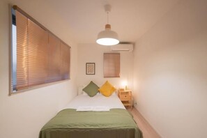 A bedroom with a bed, bedside table, lamp, and window blinds. - Travel Time - Senbon Naka (Osaka)