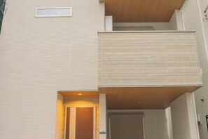 A modern building with a flat facade, a visible entrance, and a balcony.