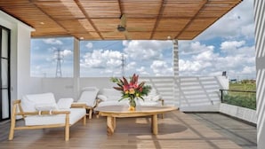 An outdoor patio with a wooden ceiling, white furniture, and a table with a floral centerpiece.