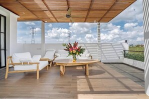 An outdoor patio with a wooden ceiling, white furniture, and a table with a floral centerpiece.