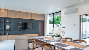 A modern kitchen with a built-in oven, a dining area with a long table and chairs, and a large window with a view of greenery.