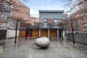 A courtyard with a large spherical sculpture, trees, and buildings with wooden doors.