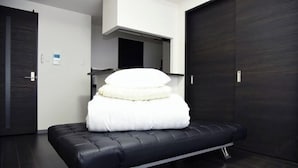 Una habitación moderna con un sofá cama negro, una almohada blanca y un piso de madera oscura.
