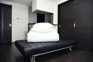 A modern room with a black sofa bed, a white pillow, and a dark wooden floor.