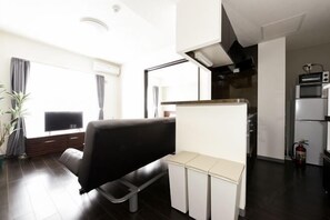 A modern living room with a sofa, a television, and a kitchen area with appliances.