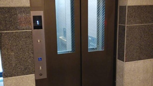 Un ascensor con pantalla digital, símbolo de accesibilidad para sillas de ruedas y panel de vidrio.