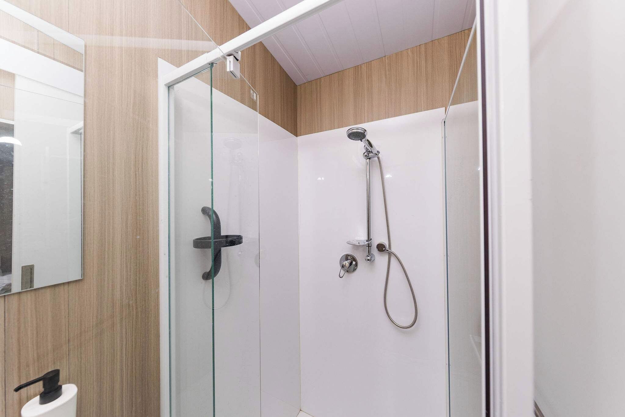 Una cabina doccia in vetro con doccetta e rubinetto a mano.