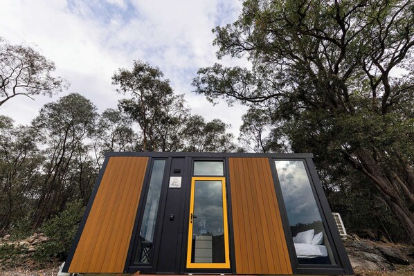 A modern cabin with a large window and a door, surrounded by trees.