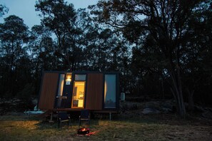 A small cabin with a wooden exterior, a glass door, and a fire pit outside.