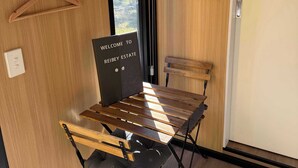 A room with a wooden table, chairs, a hanging coat rack, a welcome sign, and a small electronic device on the wall.