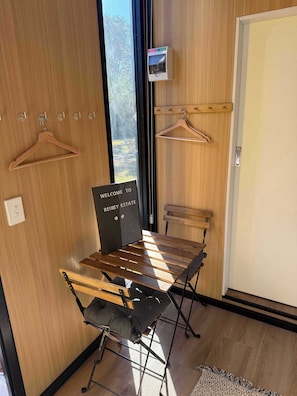 Una habitación con una mesa de madera, sillas, un perchero colgante, un cartel de bienvenida y un pequeño dispositivo electrónico en la pared.