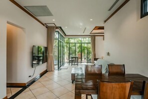 A modern dining area with a wooden table and chairs, a flat-screen TV mounted on the wall, and a sliding glass door leading to an outdoor space.