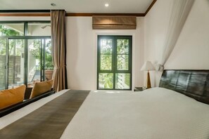 A hotel room with a large bed, a window with curtains, a nightstand, and a view of greenery outside.